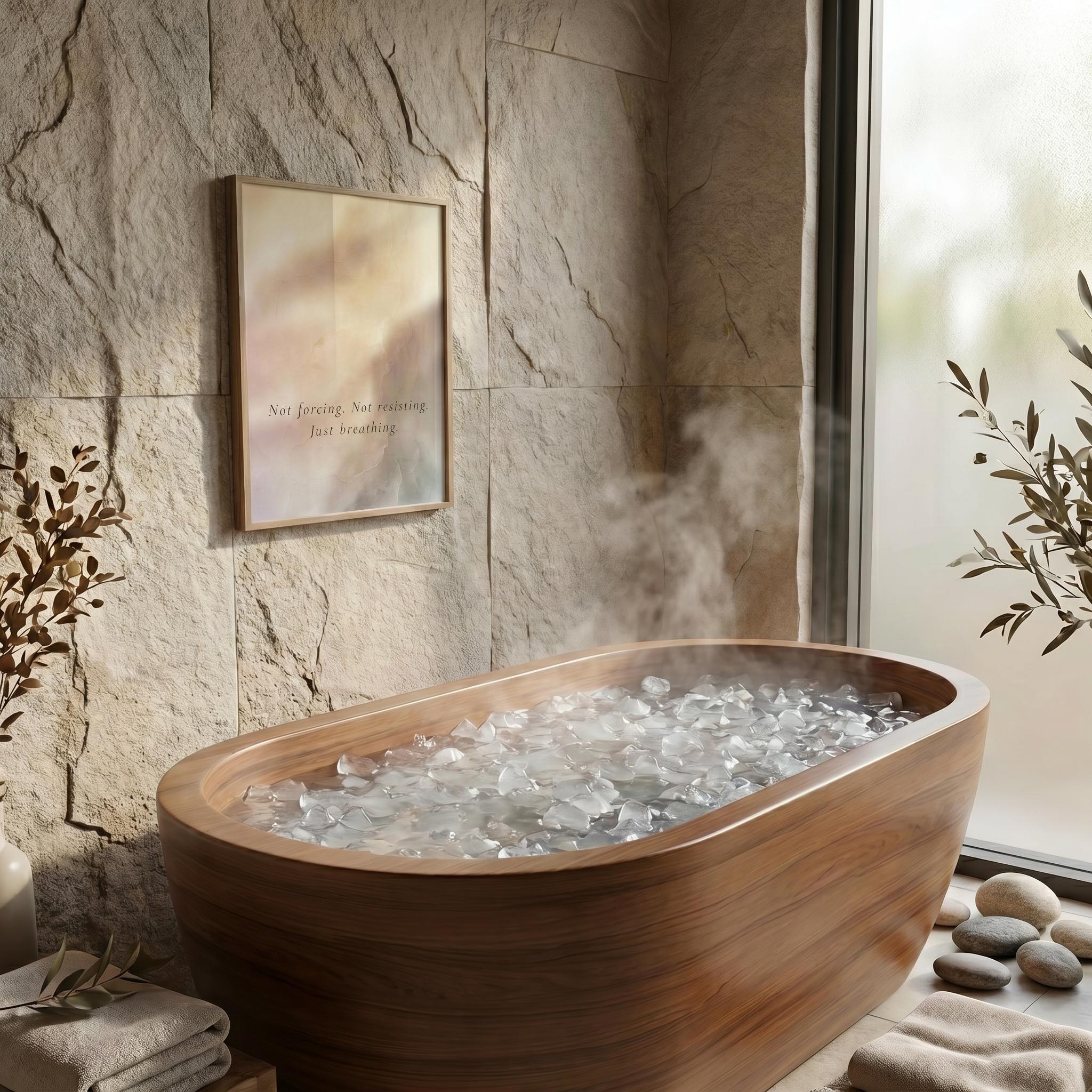A wooden freestanding bathtub filled with clear ice, placed in a spa-like bathroom setting with a stone wall, framed art, a window, and folded towels.