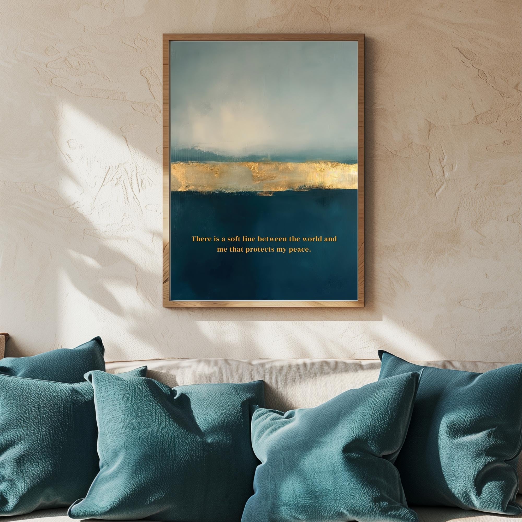 A framed abstract art print hangs on a textured beige wall above a sofa with teal pillows. The artwork features a blue and gold landscape with a quote in gold text at the bottom.